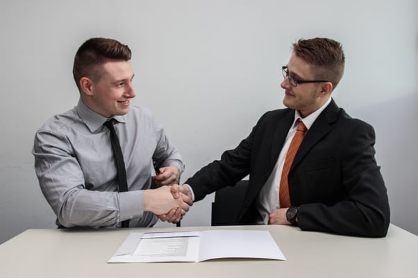 Two men shaking hands at desk - How to write a copywriting brief template - Copify blog 2
