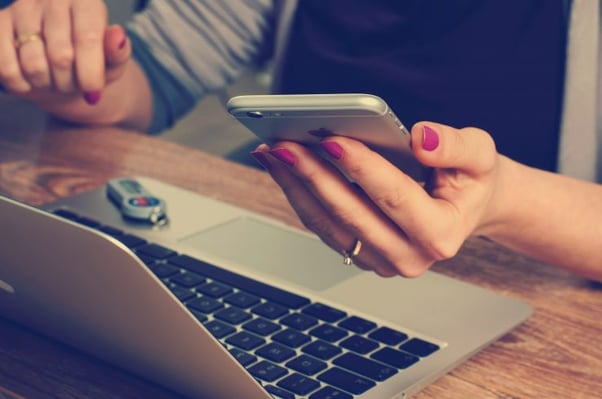 Woman using iphone and laptop - A day in the life of a copywriter - Copify Blog