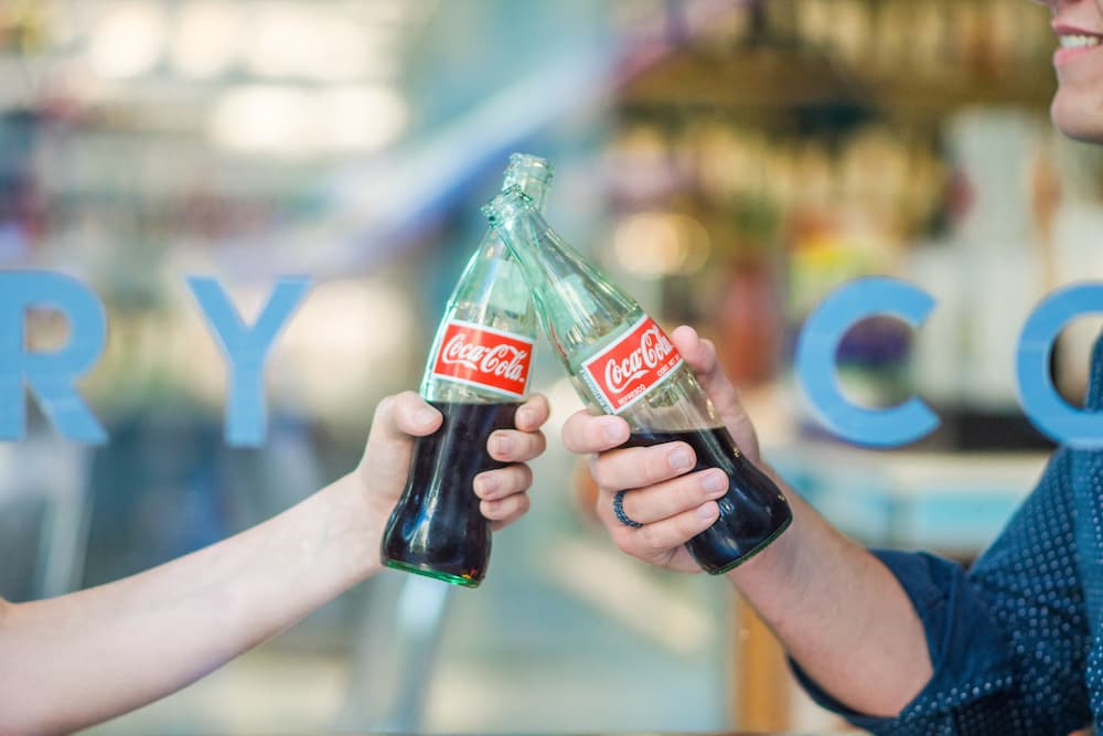 Two people clinking Coca-Cola bottles - 4 of the best marketing gimmicks of all time - Copify Blog