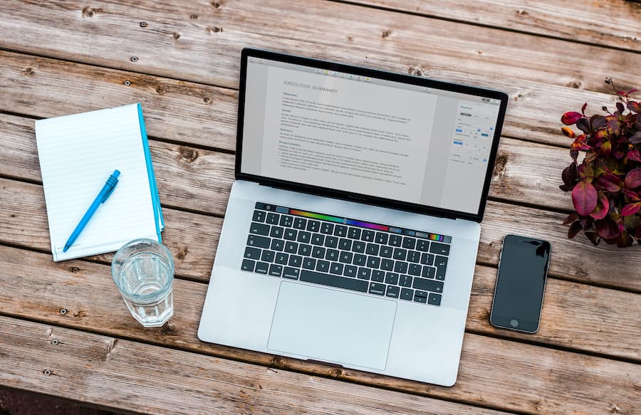 Laptop open on a table outside with notebook and phone - 5 online copy editing training courses 2020 - Copify blog