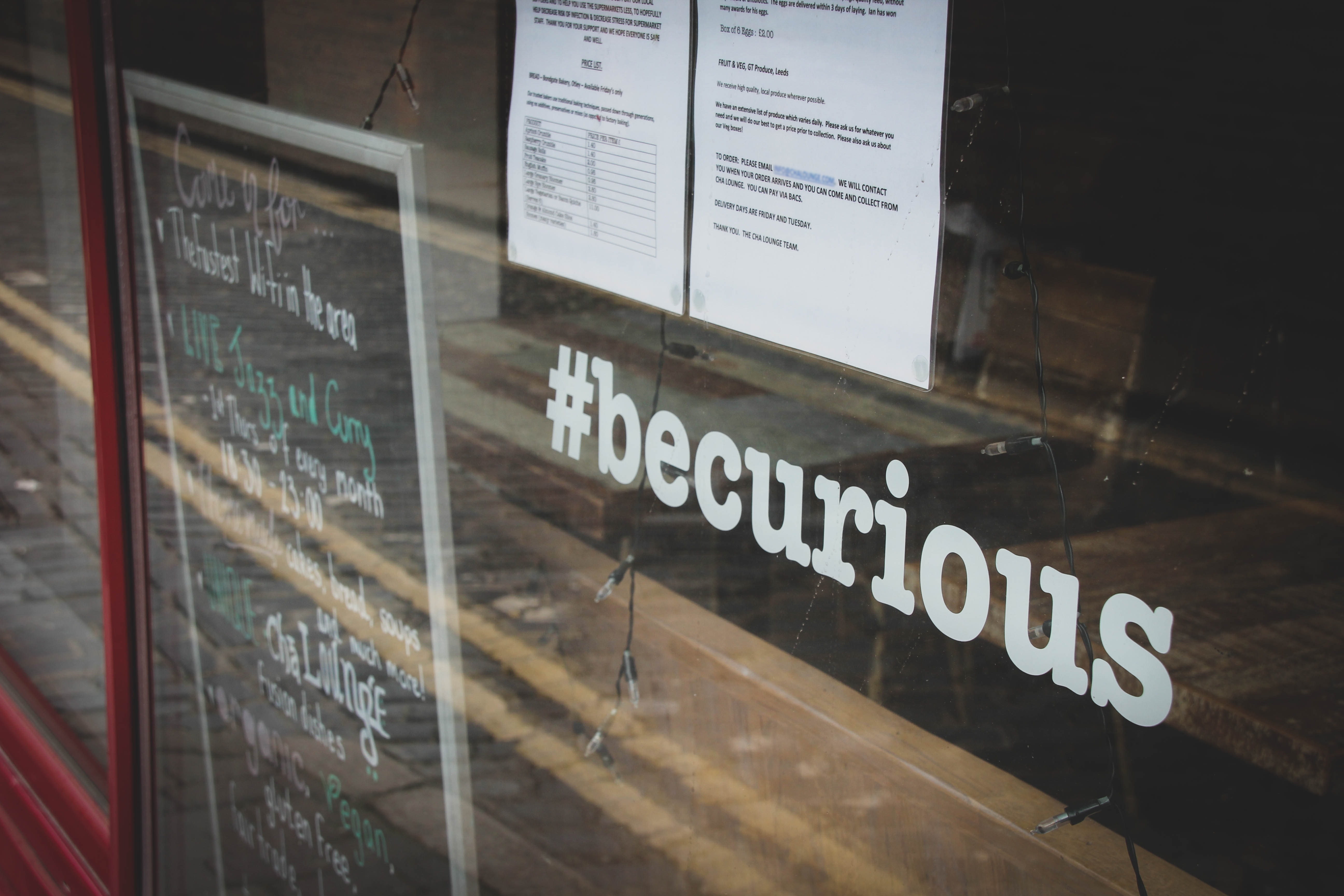 Sign in cafe window that says #becurious - 6 rules to follow to develop killer copywriting skills - Copify Blog
