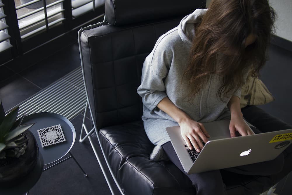 Woman in leather chair on laptop - Are you copy writing or copywriting? - Copify blog